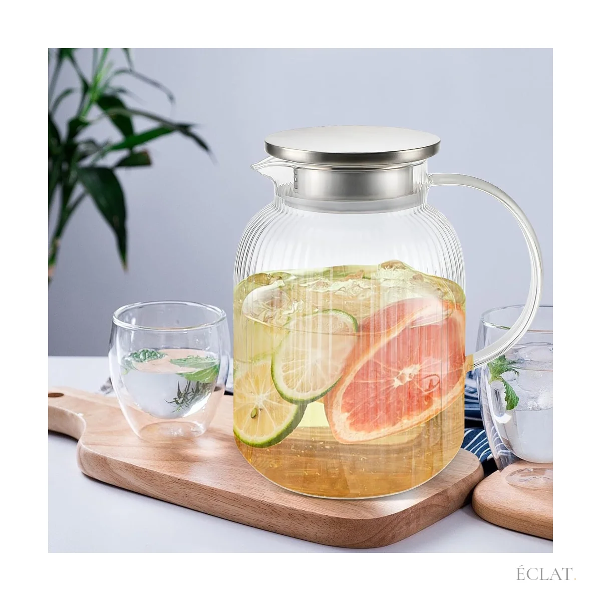 Pichet à eau en verre strié et couvercle inox servi avec agrumes et verres sur une planche en bois