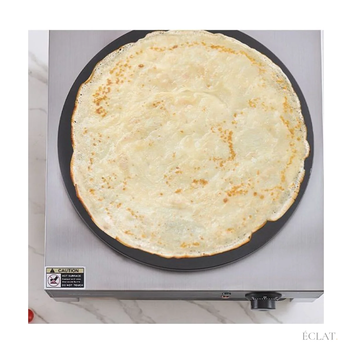 Grande crêpe dorée en cuisson sur une crêpière électrique ronde